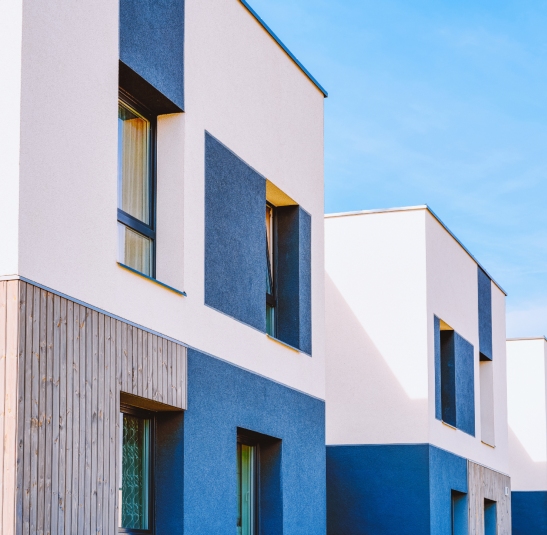 Façades de bâtiments modernes avec murs blancs, panneaux bleus et bardage en bois sous un ciel bleu dégagé