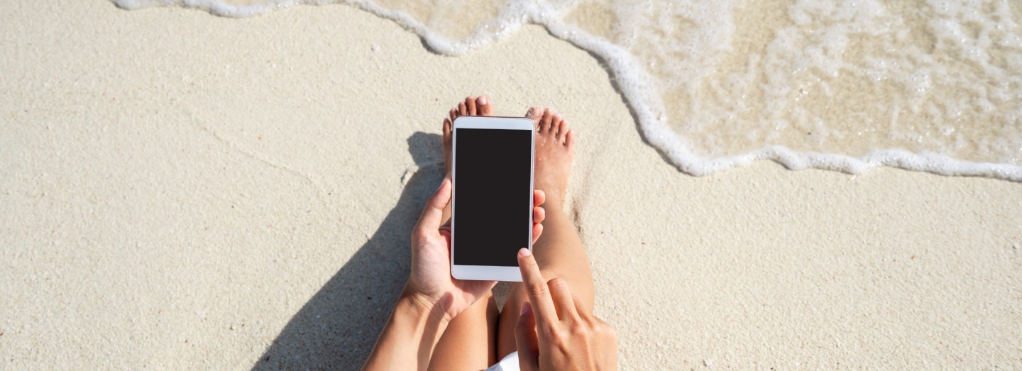 Personne utilisant un smartphone sur une plage de sable au bord de l’eau