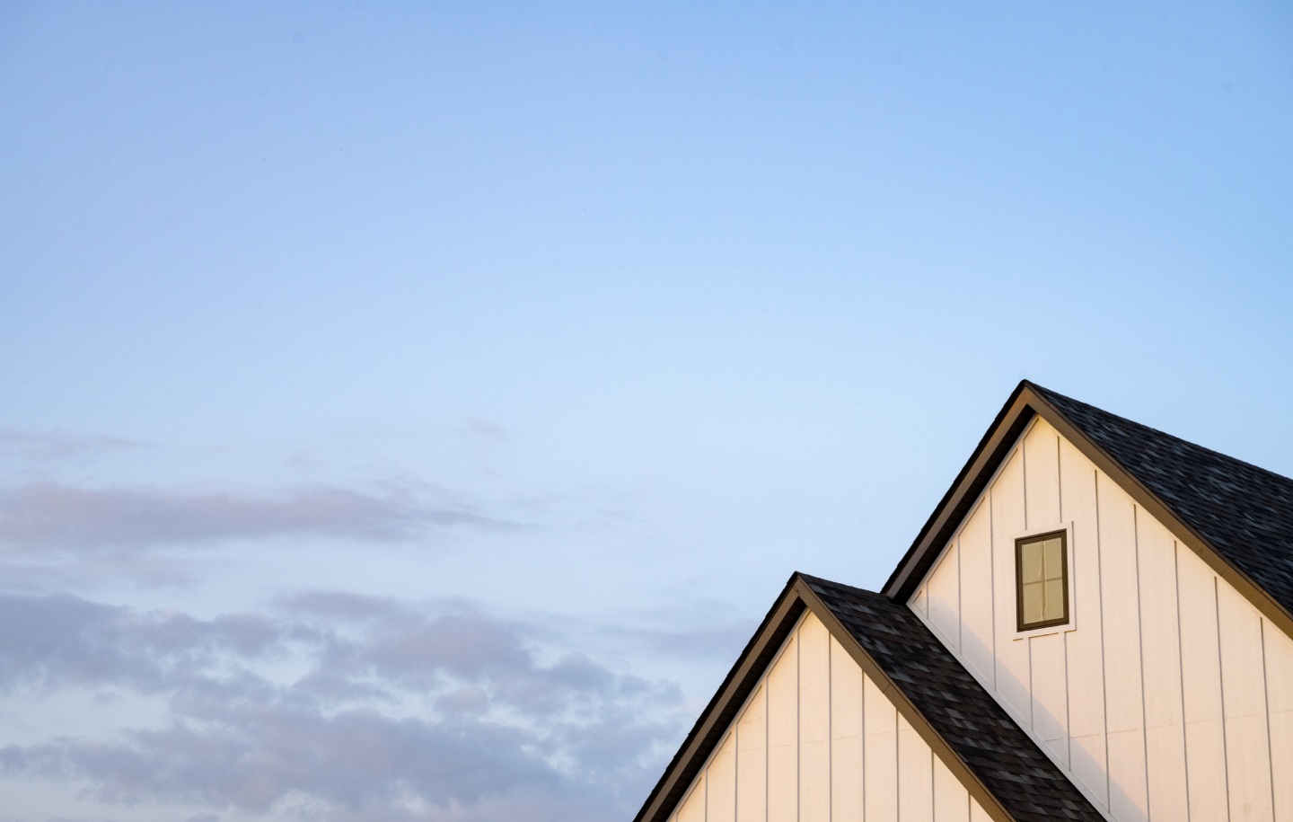 Maison contemporaine blanche avec toiture à pignons sous un ciel bleu aux nuages légers